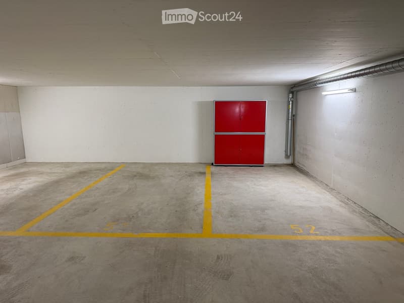 Empty underground garage with concrete floor, white walls, red storage cabinet, and yellow parking lines marked '51' and '52'.