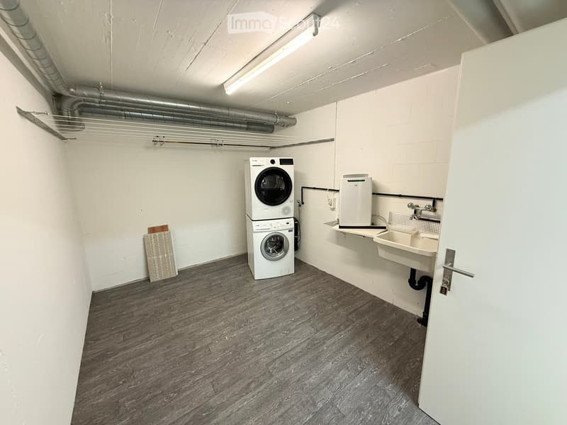 A small utility room with a washing machine, dishwasher, and sink, featuring white walls and a wooden floor.