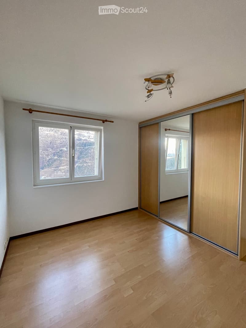 Empty room with light wooden flooring, white walls, large window with view, and sliding mirrored door.