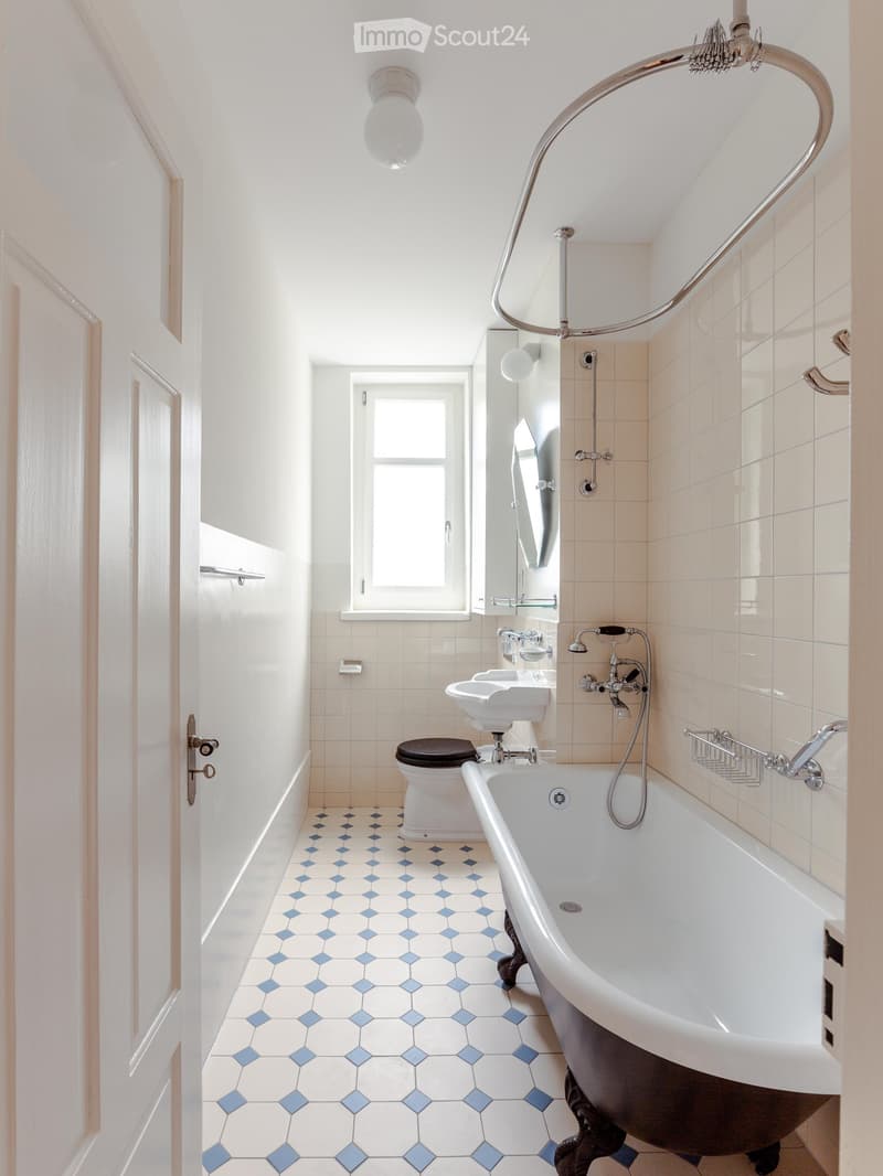 Bathroom with a white bathtub, toilet, sink, mirror, and a window. The floor has blue and white hexagonal tiles.