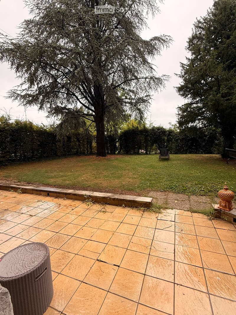 Garden with tiled patio, grassy lawn, large tree, and outdoor furniture.
