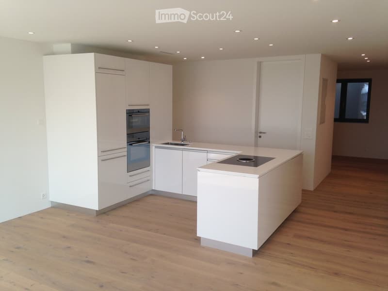 Modern kitchen with white cabinets, a central island, an induction cooktop, and a sink with a faucet. The floor is made of light wooden planks.