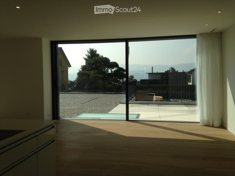 Bright, unfurnished room with wooden flooring, large glass sliding doors opening to a terrace with a swimming pool and scenic mountain view.
