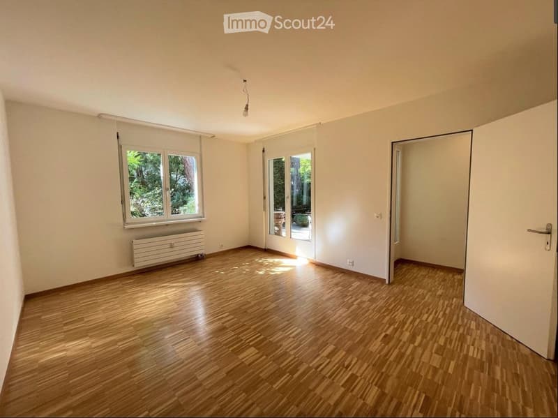 Empty room with wooden flooring, white walls, large windows, and a radiator. No furniture or equipment present.