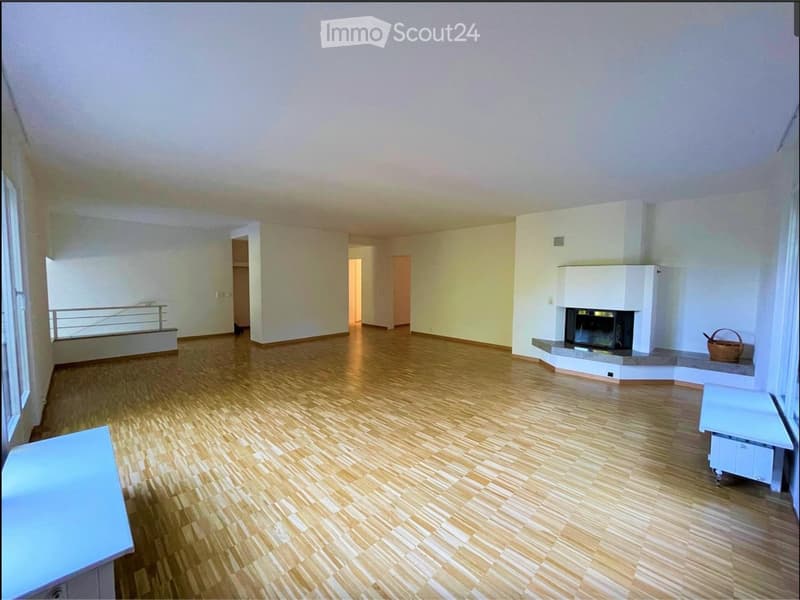 Empty living room with wooden flooring, white walls, fireplace, and large windows with a balcony view.