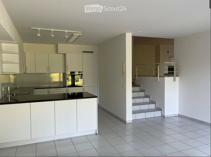 Modern kitchen with white cabinets, black countertop, and a staircase leading to an upper level.