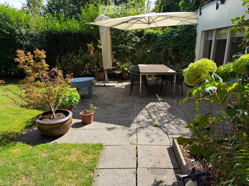 A well-maintained garden patio with a table, chairs, umbrella, and various potted plants.