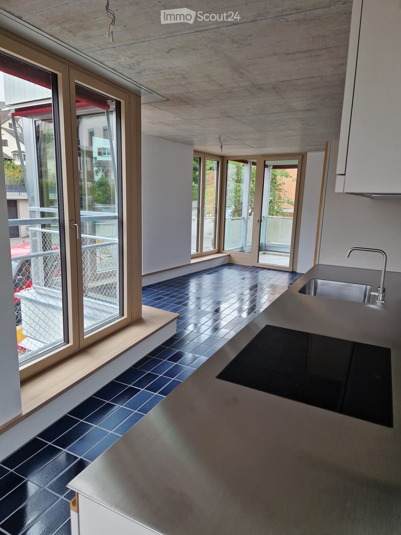 Modern kitchen with dark blue tiles, sleek countertops, and large windows leading to a balcony.