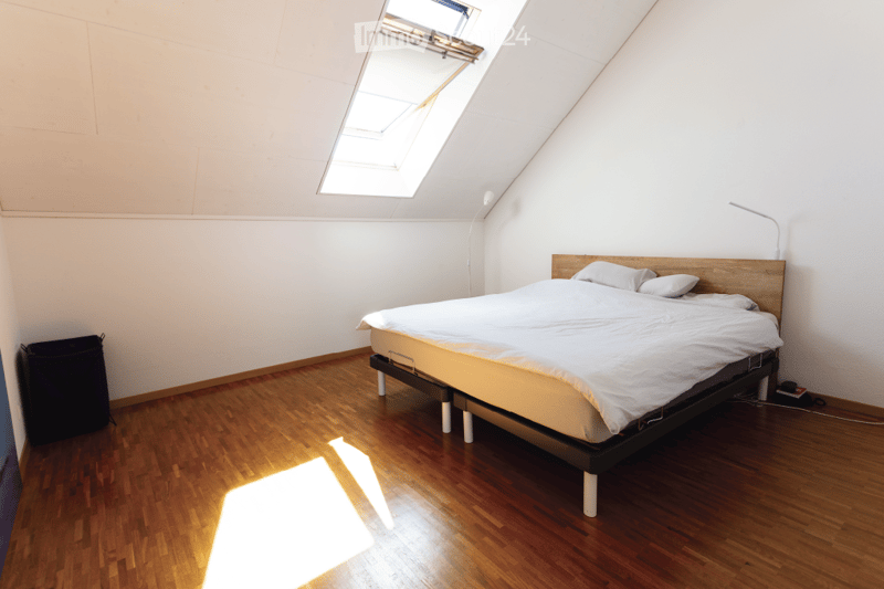 Bright, minimalist bedroom with wooden flooring, a single bed with white linens, a modern bed frame, and a skylight window allowing natural light to flood the space.