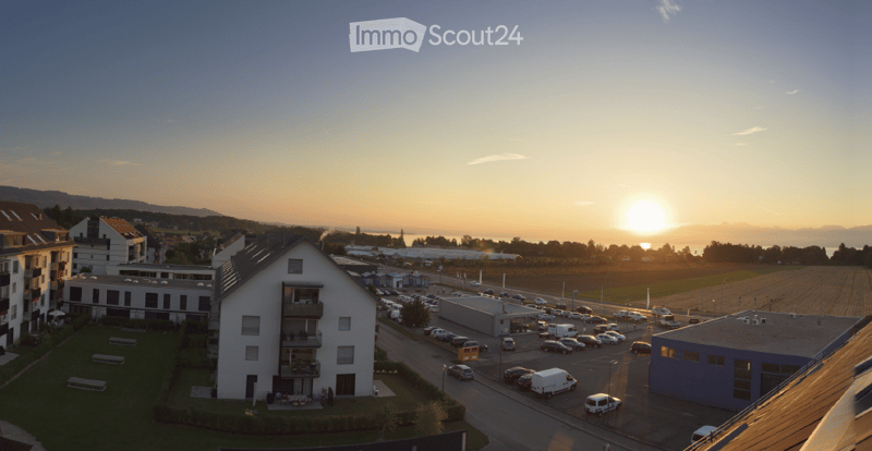 Aerial view of a residential area at sunset, showing multiple buildings, parking lots, and a road with vehicles.