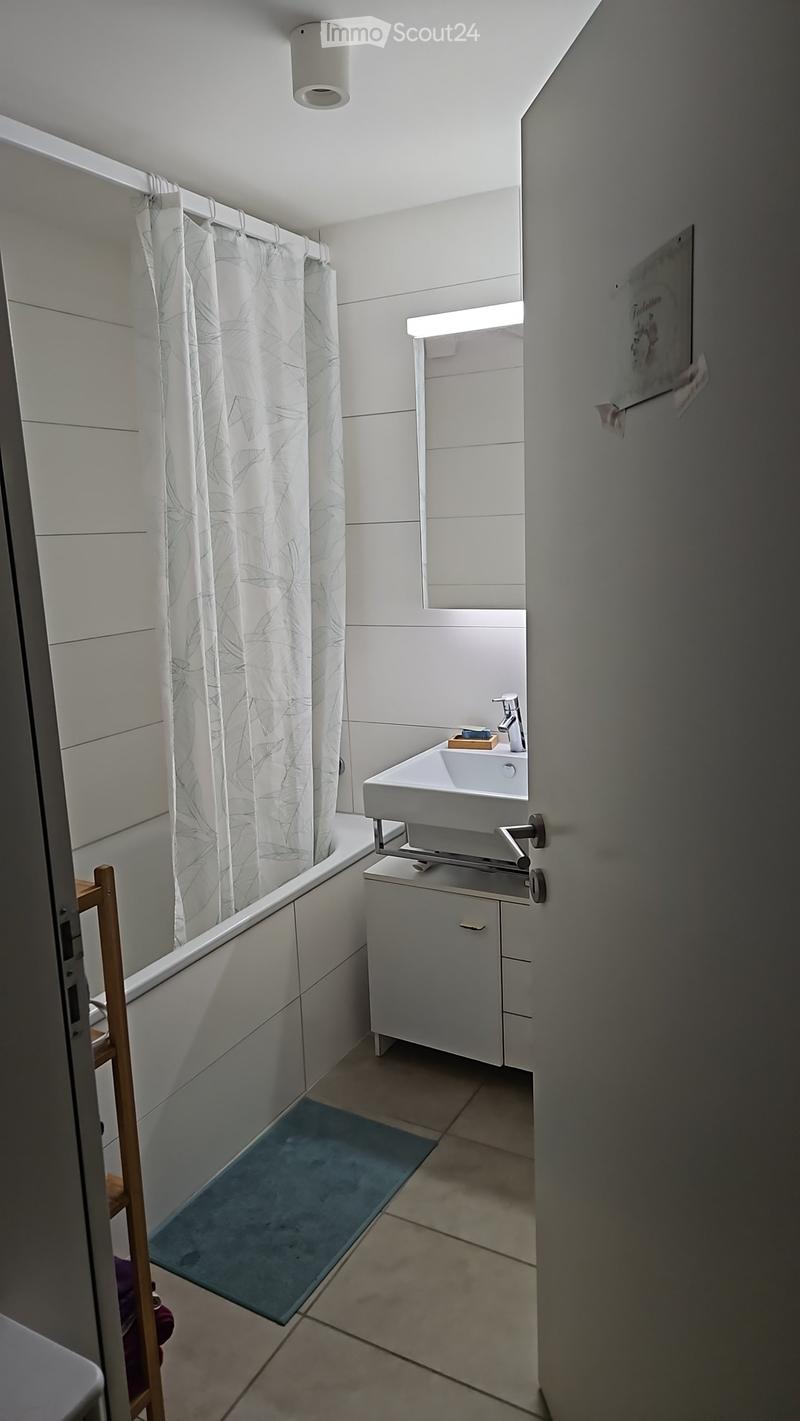 Modern bathroom with a white bathtub, sink, and cabinet. Features a leaf-patterned shower curtain and a blue bathroom rug.
