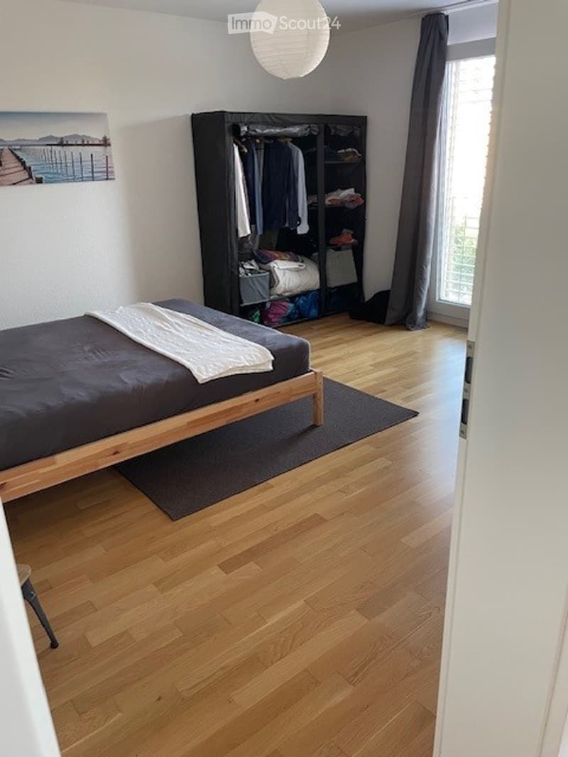 Bedroom with wooden flooring, a bed with dark bedding, a wardrobe, and a picture frame on the wall.