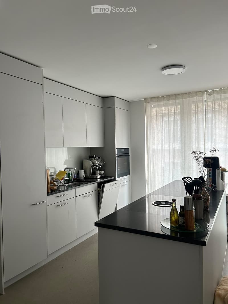 Modern kitchen with white cabinets, black countertop, stainless steel appliances, and various kitchen items on the counter.