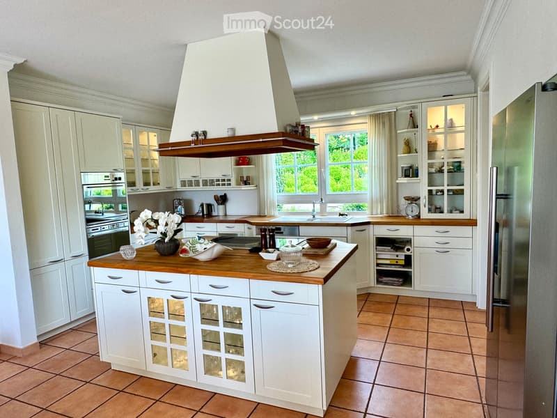 white cabinets, wooden island, dishwasher, integrated fridge, stainless steel hood, gas stove, sink, tiled floor