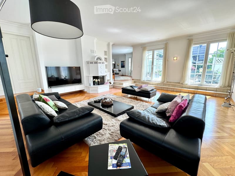 Large living room with fireplace, black leather sofas, center table, TV, white curtains, hardwood floor, view