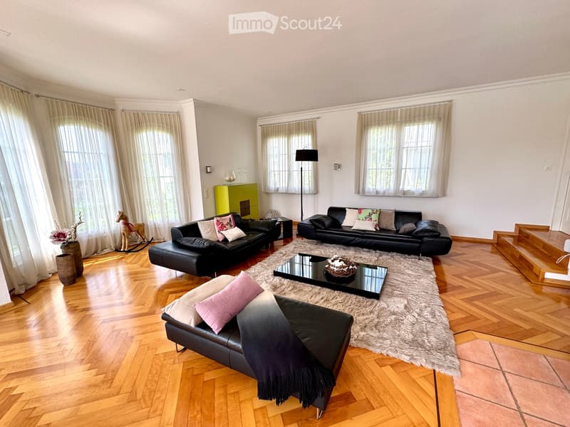 modern, large living room, parquet floor, beige rug, modern black leather sofa, black coffee table, two white vases with flowers, wooden stairs