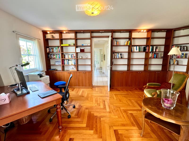 wooden desk, black chair, keyboard, monitor, wooden shelves, wooden floor, lamp, books