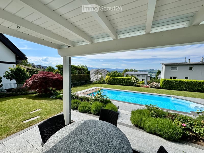 Outdoor dining area with table and chairs, swimming pool, well-maintained garden, distant houses and mountains