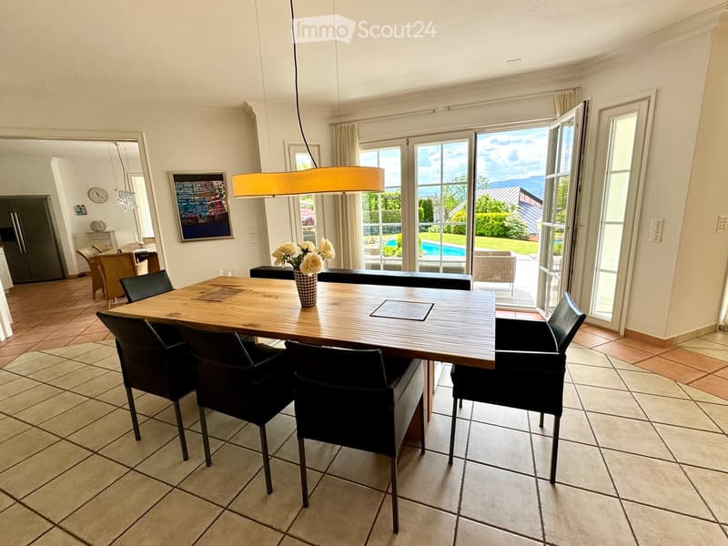 large wooden table, black chairs, vase with flowers, open terrace, swimming pool view