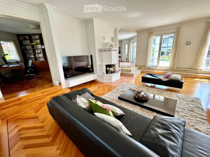 Modern living room with black leather sofa, coffee table, rug, television, bookshelf, and fireplace.