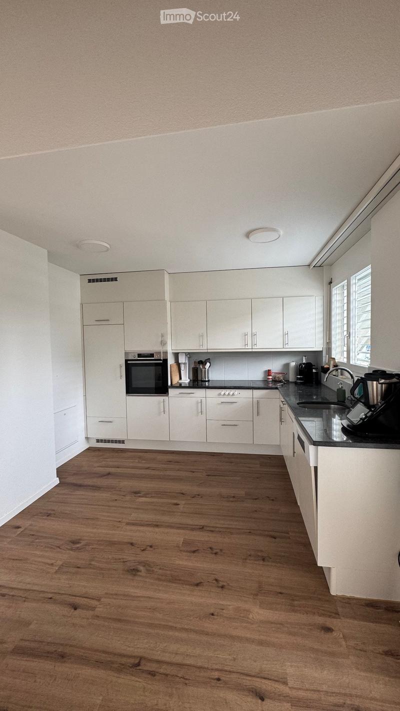 Modern kitchen with white cabinets, wooden flooring, and stainless steel appliances including an oven and coffee maker.