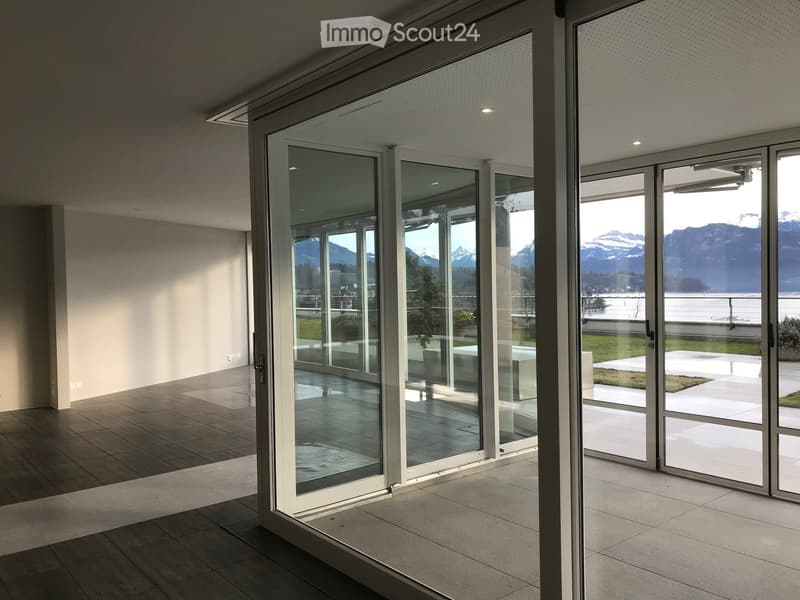Modern hallway with large glass sliding doors leading to a scenic outdoor area, featuring a tiled floor and white walls.