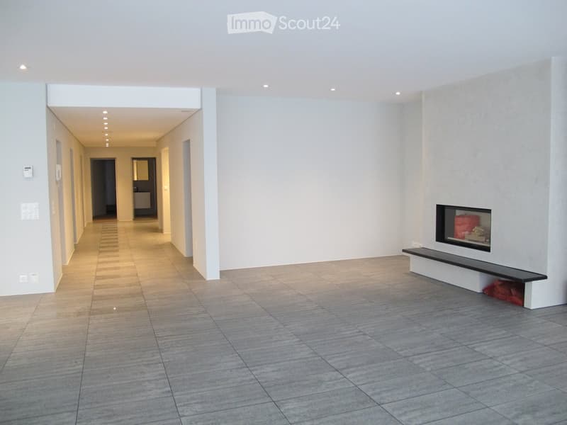 Empty hallway with tiled floor, white walls, recessed lighting, and a built-in fireplace with a bench on one side.