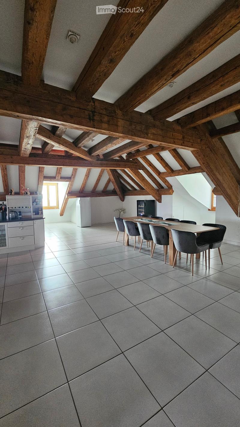 Open-plan dining and kitchen area with exposed wooden beams, tiled floor, and modern furniture.