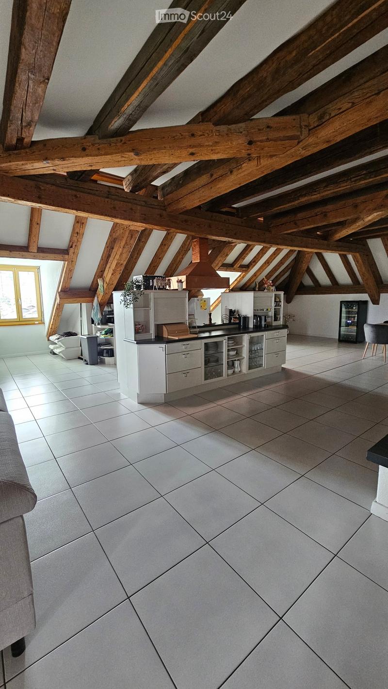 Modern kitchen with white cabinets, stainless steel appliances, and a large window. The space features exposed wooden beams on the ceiling and a tiled floor.