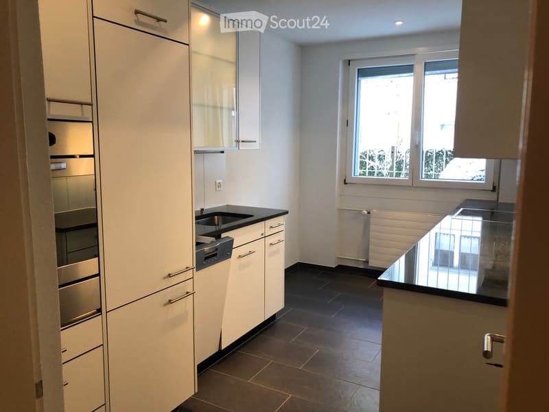 Modern kitchen with white cabinets, stainless steel appliances, dark countertops, and a black tiled floor.