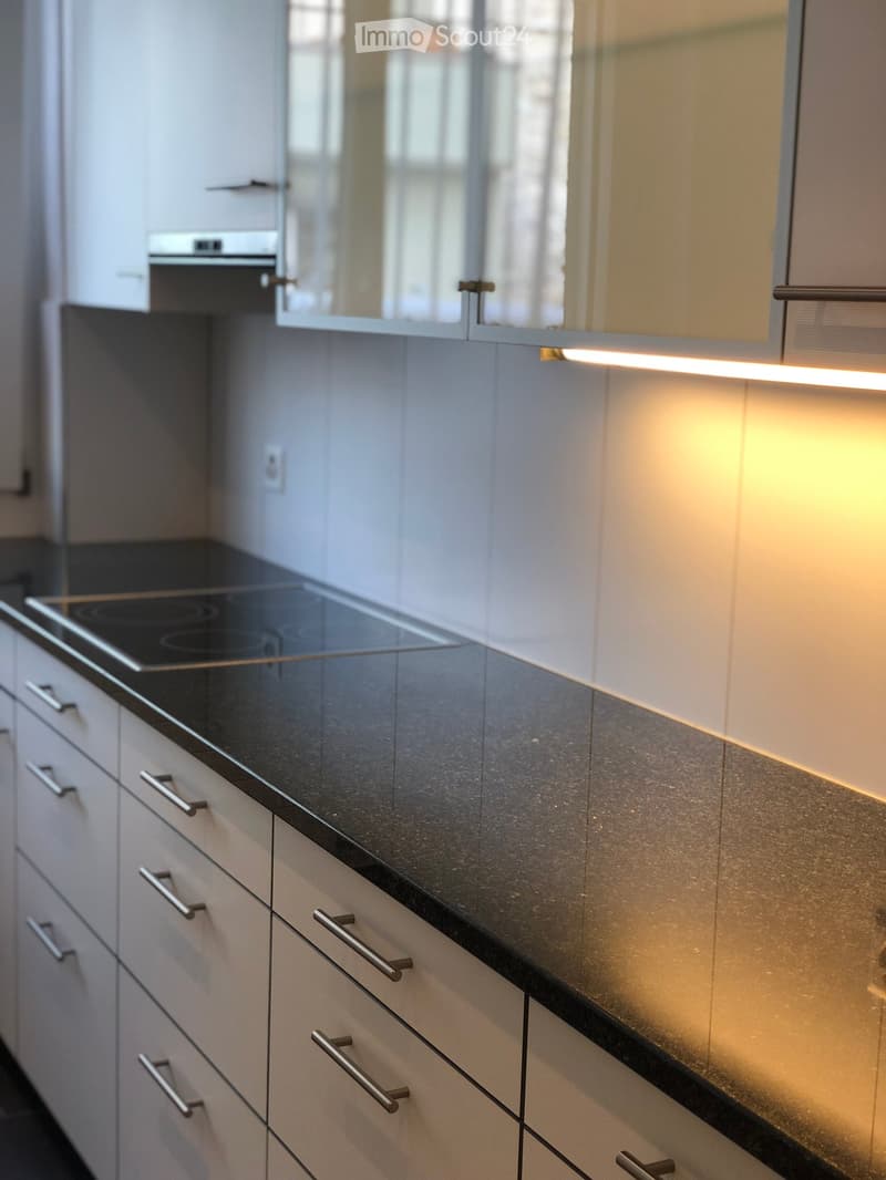 Modern kitchen with white cabinets, black countertop, and built-in induction cooktop. Features sleek stainless steel handles and ambient lighting.