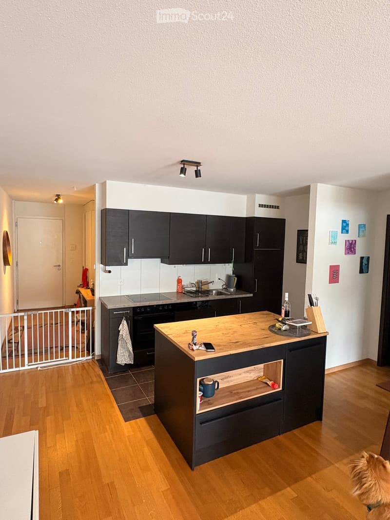 Modern kitchen with dark cabinets, wooden countertop, sink, and various appliances. Includes a small island with open shelving and a few items on the counter.