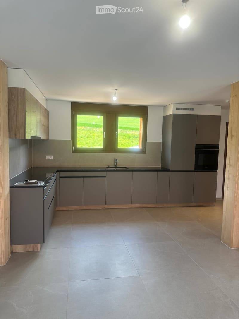 Modern kitchen with grey cabinets, a central island, and a window overlooking a green area.