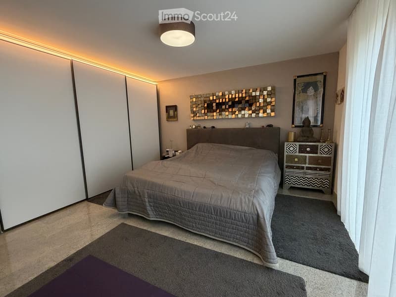Modern bedroom with a large bed, nightstand, decorative mirror, artwork, and a stylish lamp.