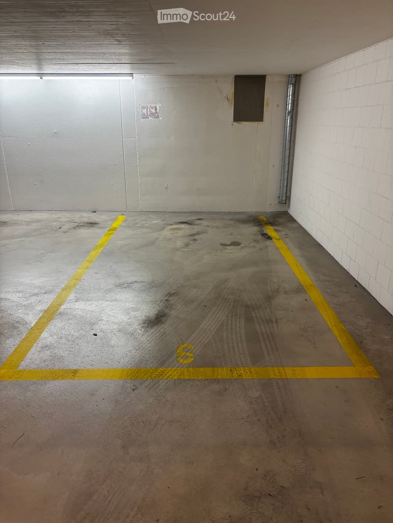 Empty underground parking space with concrete floor, yellow parking lines, and white brick walls.