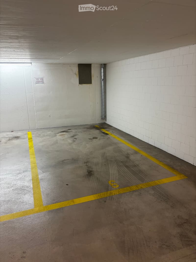 Empty underground parking space with concrete floor, white brick walls, and yellow parking lines.