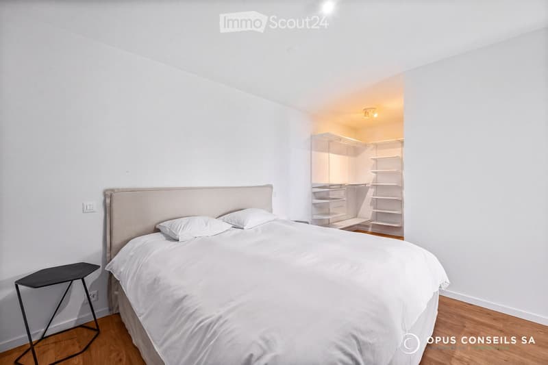 Modern bedroom with a large bed, white bedding, a nightstand, and an open wardrobe with shelves.