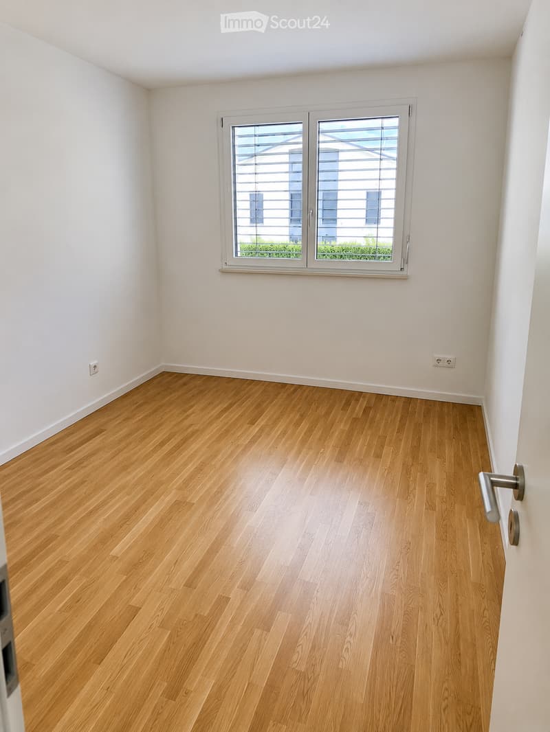 Empty room with light wooden flooring, white walls, and a large window with blinds. No furniture or equipment present.
