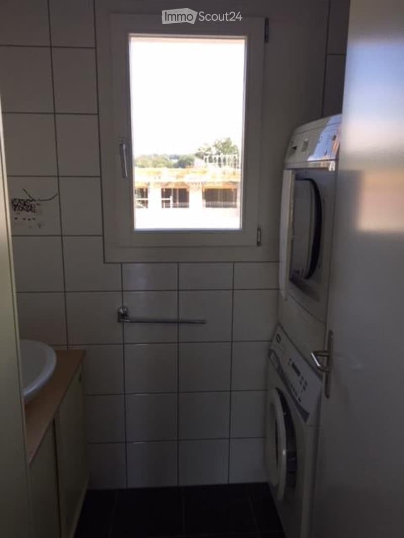 Bathroom with tiled walls and floor, a window, a washing machine, and a sink.