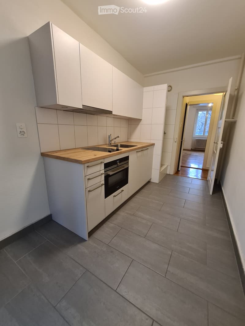 Modern kitchen with white cabinets, wooden countertop, sink, and built-in oven. The space is clean and well-lit, with a hallway leading to another room visible in the background.