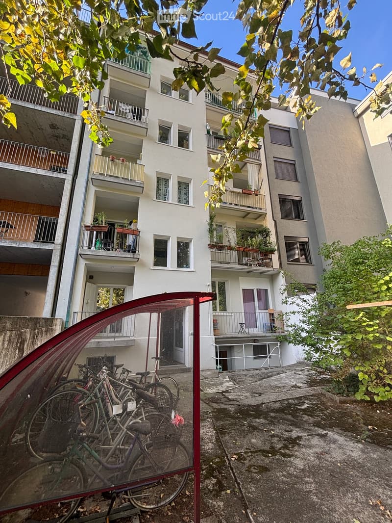 Multi-story residential building with balconies, windows, and greenery. Bicycles are parked in the foreground.