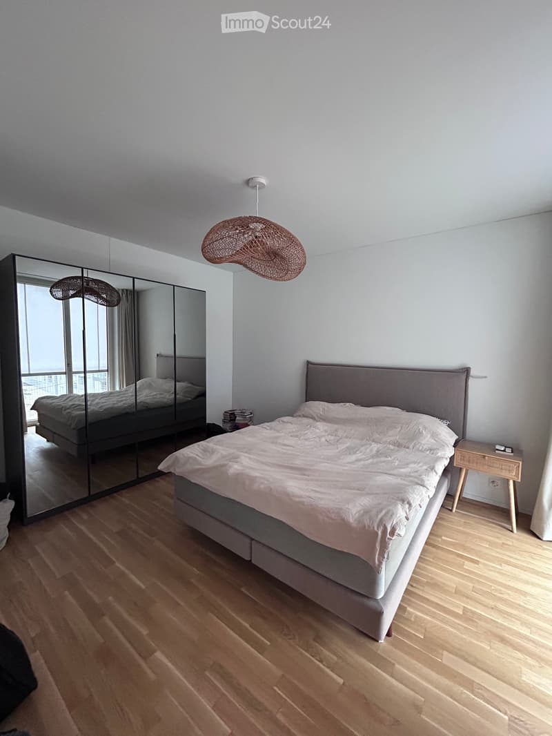 Modern bedroom with a large bed, wooden floor, large mirror, and pendant light fixture.