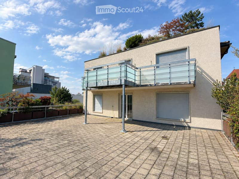 Modern two-story house with a balcony, garage, and surrounding greenery.