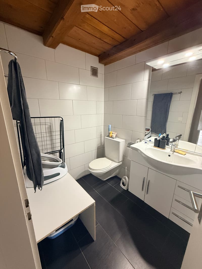 Modern bathroom with white tiles, dark grey floor, toilet, sink, mirror, and cabinet.