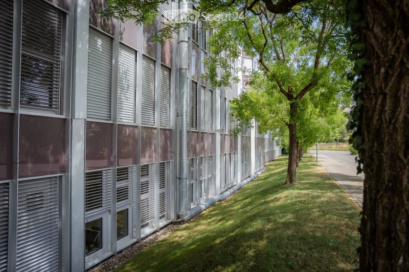 Modern building with a sleek, contemporary design featuring large windows and metallic accents, surrounded by a well-maintained lawn and trees.