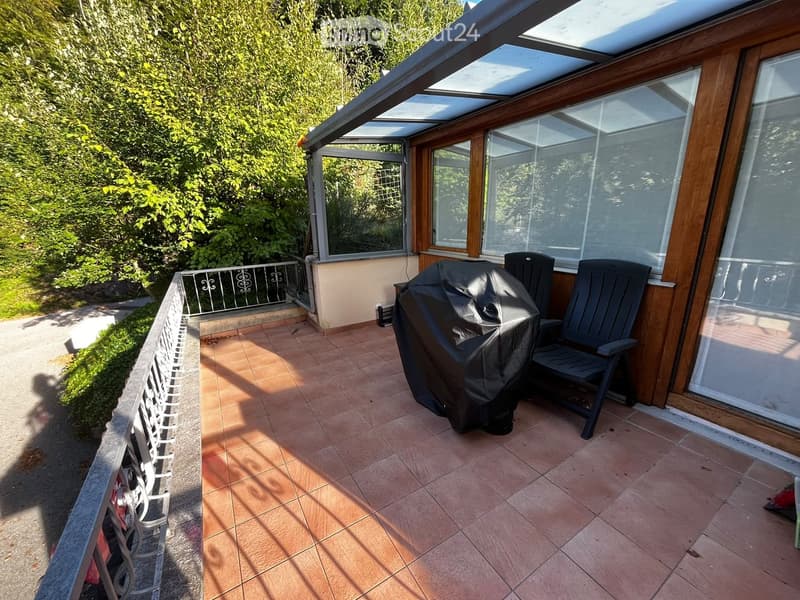 Balcony with tiled floor, covered area, grill, and chairs.