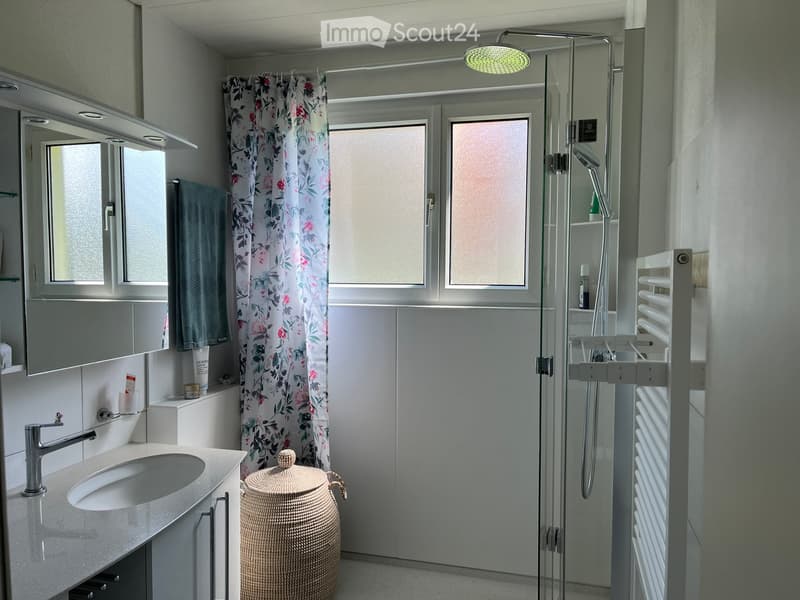 Modern bathroom with a sink, mirror, shower, and radiator. Features a wicker basket and a floral shower curtain.