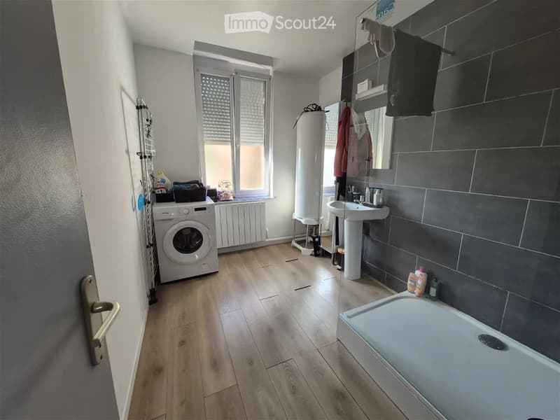 Bathroom with wooden flooring, a sink, bathtub, washing machine, radiator, and a mirror. The room is well-lit with natural light from a window.