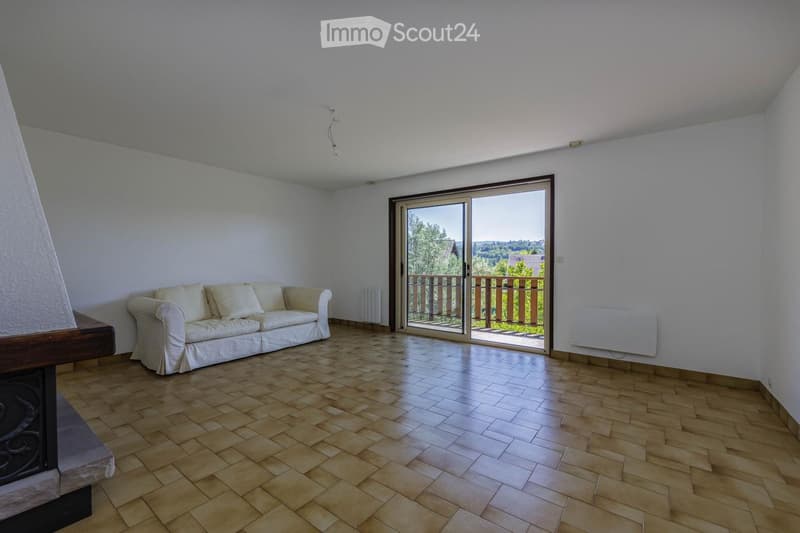 Bright living room with wooden tiled flooring, white walls, a cream-colored sofa, and a sliding glass door leading to a balcony.