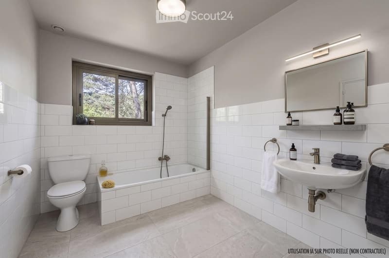 Modern bathroom with white tiles, a bathtub, toilet, sink, mirror, and decorative bottles on the shelf. Features a window with a view of greenery outside.